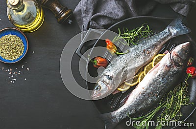 Ingredients for cookig healthy fish dinner. Raw uncooked seabass with olive oil, herbs and spices on black grilling Stock Photo