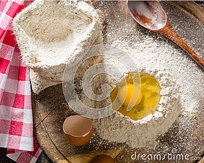 Ingredients for cooking dough or bread. Broken egg on top of a bunch of white rye flour. Dark wooden background. Stock Photo