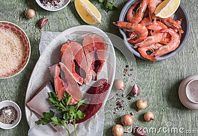 Ingredients for cooking lunch - fresh red fish, shrimp, rice, spices. On a wooden table, top view. Stock Photo