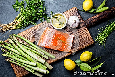 Ingredients for cooking. Raw salmon fillet, asparagus and herbs on wooden board. Food cooking background with copy space Stock Photo