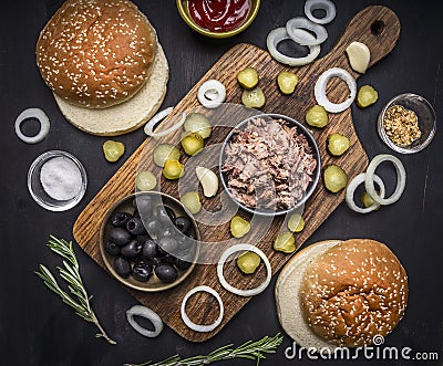 Ingredients for home kuking burger with tuna, pickled cucumbers, onions, olives and sauce on a cutting board on wooden rustic back Stock Photo