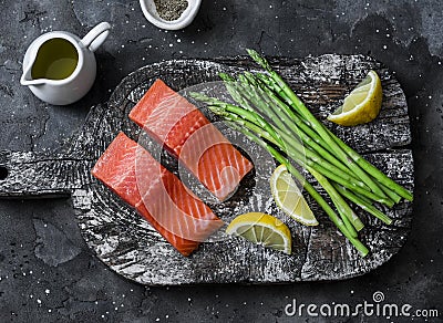 Ingredients for lunch - fresh raw organic salmon, green asparagus on a cutting board on a dark background, top view Stock Photo