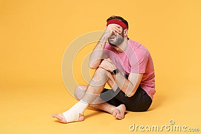 Ingured crying fitness guy sportsman in headband t-shirt in home gym isolated on yellow background. Workout sport Stock Photo