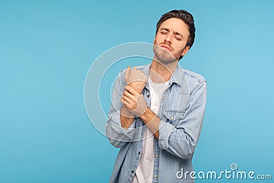 Injured arm. Portrait of office worker man in denim shirt touching painful hand, suffering trauma, sprain wrist Stock Photo