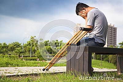 Injured Man with crutches sitting on a bench Stock Photo