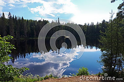 Inland lake of glacial origin on sunny day. Reflection of forest and clouds in the water. Karelian nature in the summer. Stock Photo