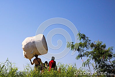 Burmese man with family carry a huge heavy sack on head through rural landscape Editorial Stock Photo