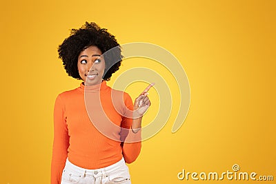 An inquisitive young woman with afro hair points upwards while wearing a bright orange sweater Stock Photo