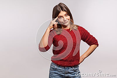 Insane idea! Portrait of girl in shaggy sweater makes stupid gesture with finger near head, out of mind, reckless Stock Photo