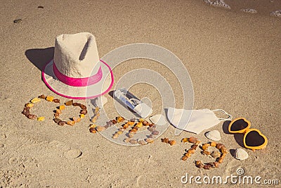 Inscription Covid-19, protective mask, disinfectant liquid for disinfection hands and sunglasses with straw hat on beach. Holidays Stock Photo