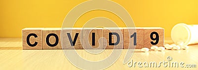 Inscription COVID19 on wooden cubes on a yellow background with pills Stock Photo