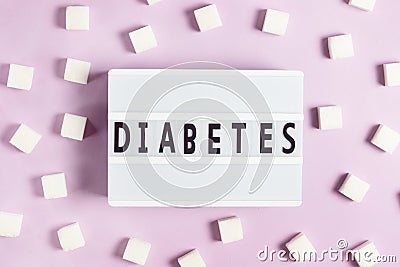 The inscription diabetes on a white board on a pink background with cubes of white sugar Stock Photo