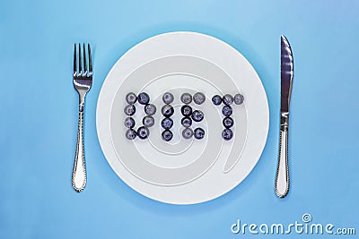 Inscription Diet made of blueberries on white plate with cutlery. Light blue background. Flat lay. Top view Stock Photo