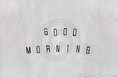 Inscription Good morning, composed of black letters on transparent plastic bases on white rumpled sheets. Top view, flat lay. Stock Photo