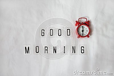 Inscription Good morning, red analog clock on white rumpled sheets. Top view, flat lay. Horizontal. Concept of rest, awakening, Stock Photo