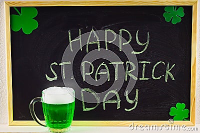 The inscription with green chalk on a chalkboard: Happy St. Patrick's Day. Clover leaves. A mug with green beer. Stock Photo