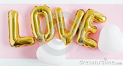 Inscription LOVE foil inflatable golden ballon on the pink background with white hearts. Love, romance and Valentines day concept Stock Photo