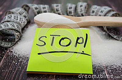 The inscription `stop` on a yellow sticker on the background of sugar and a measuring tape. Side view. Wood background. The concep Stock Photo