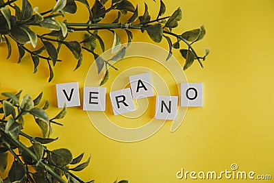 The inscription verano in spanish on the letters of the keyboard on a yellow background with branches of flowers Stock Photo