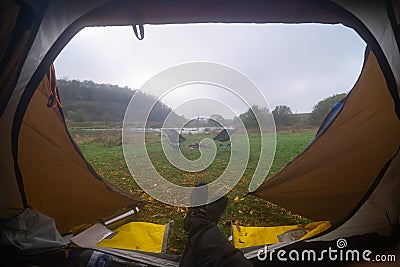 Inside the tourist tent, first person view. Foggy morning near the river. Folding chair and table. Tourism and hobby. Man legs Stock Photo