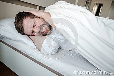 Insomnia. Man is stress, he irritably covers ears with hands and cannot fall asleep due to noise. Mental health concept. Stock Photo