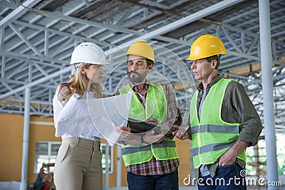 Inspector holding blueprint and looking at workers in hard hats Stock Photo
