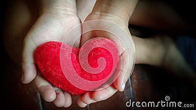inspirational love concept - image of red heart shaped pillow on kid& x27;s hands in vintage background Stock Photo