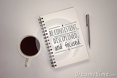 Inspirational motivational quote - Be consistent, disciplined and focused. Text message on a spiral notebook with pen, coffee cup. Stock Photo