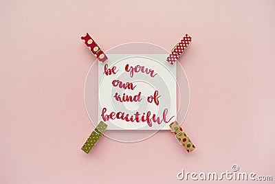 Inspirational quote be your own kind of beautiful handwritten with watercolor in calligraphy style, miniature clothespins on a pal Stock Photo