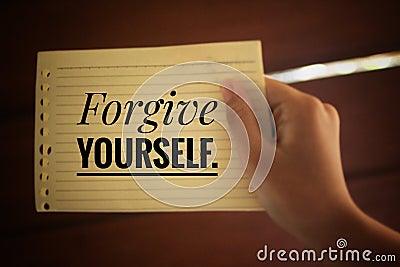 Inspirational quote - Forgive yourself. With a paper note in young woman hand on light brown background. Reminder and note to self Stock Photo