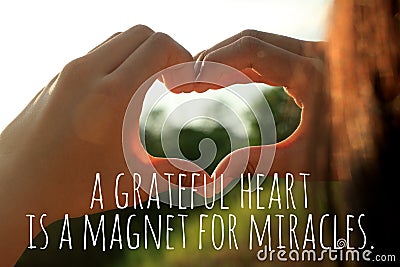 Inspirational quote - A grateful heart is a magnet for miracles. With young woman hands making love sign against the sunset light Stock Photo