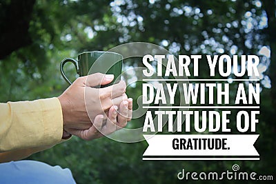 Inspirational quote - Start your day with an attitude of gratitude. With person holding a cup of tea or coffee in hands on green Stock Photo