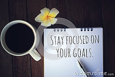 Inspirational quote - Stay focused on your goals. With text message on white paper book, pen, a cup of morning coffee, flower. Stock Photo