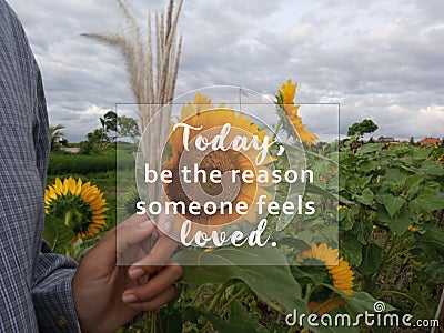 Inspirational quote - Today, be the reason someone feels loved. With blurry background of sunflowers garden, hand holding flower.v Stock Photo
