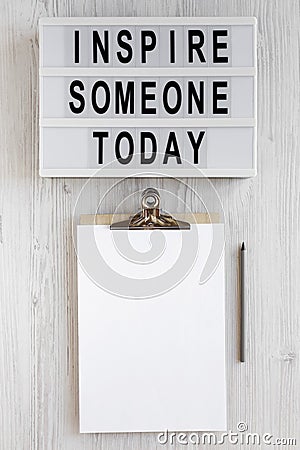 `Inspire someone today` words, clipboard with blank sheet of paper on a lightbox on a white wooden background, top view. Overhea Stock Photo