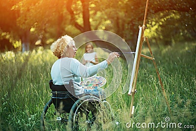 Woman in wheelchair drawing on easel outside Stock Photo