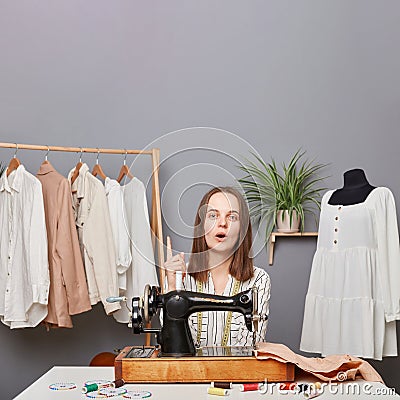 Inspired excited woman seamstress sitting at table at her workplace in atelier raising finger up having new idea for seasonal Stock Photo