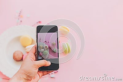 instagram blogging concept, flat lay. food photography. hand holding phone and taking photo of stylish colorful macaroons in Stock Photo
