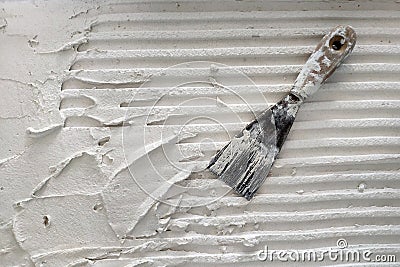 Installation of ceramic tiles. Tools for laying tiles- trowel, toothed spatula. Glue for a tile with a gear pattern. Stock Photo