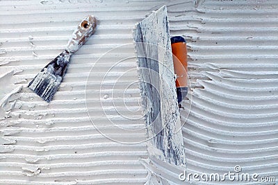 Installation of ceramic tiles. Tools for laying tiles- trowel, toothed spatula. Glue for a tile with a gear pattern. Stock Photo