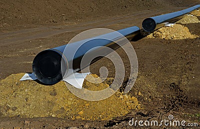 Installation of gas pipelines in field. excavated topsoil hiding route. black pipe is supported by piles of soil and is welded abo Stock Photo