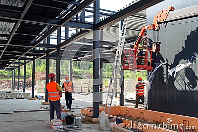 An installer in a hanging cradle and a work team are installing wall panels at the construction site of a medical aid and rescue Editorial Stock Photo