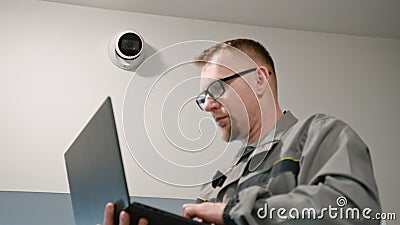 Installer in uniform sets up security camera in office room using laptop Stock Photo