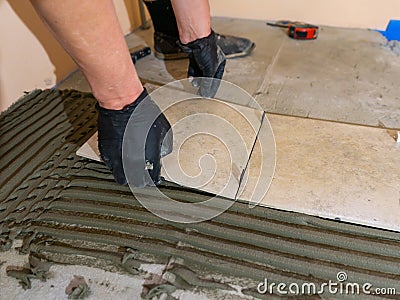 Installing ceramic floor tiles - placing the tile into the adhesive material bedding, closeup Stock Photo