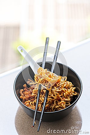 Instant noodles korean hot chili ramen stlye with pork crackink chilli paste in black bowl with chopstick Stock Photo