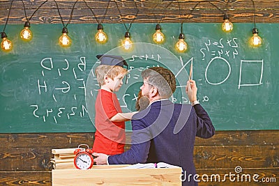 Instructive conversation concept. Teacher with beard, father teaches little son in classroom, chalkboard on background Stock Photo