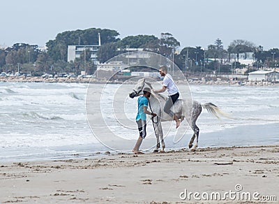 Instructor trains a young man to ride a horse on the shore of the Mediterranean Sea near the city Acre in Israel Editorial Stock Photo