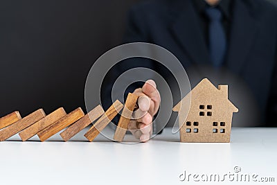 Insurance agents or family leaders are using hands to prevent Dominos from falling into the house. Stock Photo