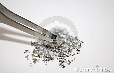 IC in tweezers above a pile of SMT components. Stock Photo