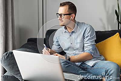 A young man with a laptop writing in a notebbook Stock Photo